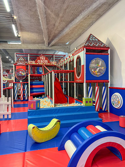 Vue panoramique de l'aire de jeux indoor Circus Kids à Vauvert avec double toboggan rouge, vastes piscines à balles et la structure tubulaire principale sur le thème du cirque installée par Play In Business.
