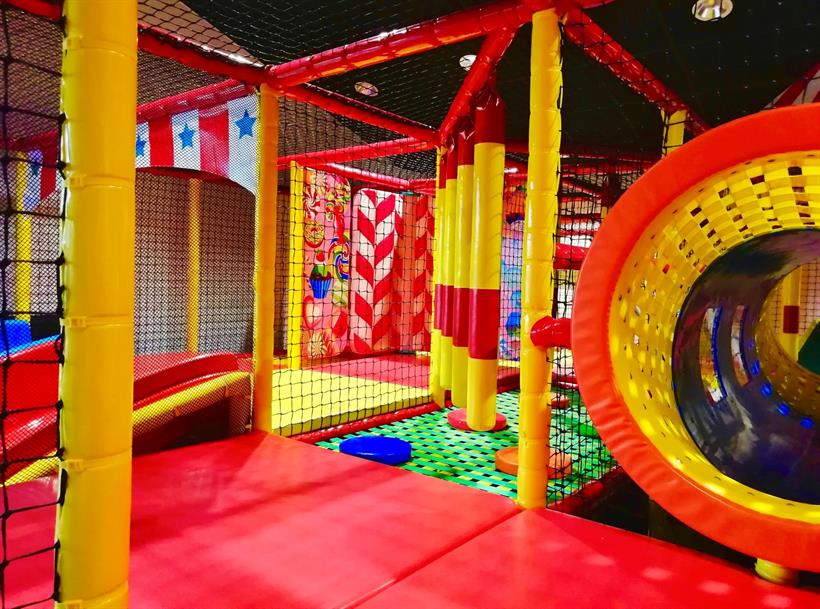 Vue intérieure du parcours d'obstacles de l'aire de jeux au BAX Bowling de Brumath aménagée par Play In Business. On y voit un tunnel, des modules de protection en mousse rouges et jaunes, et des décors muraux festifs.