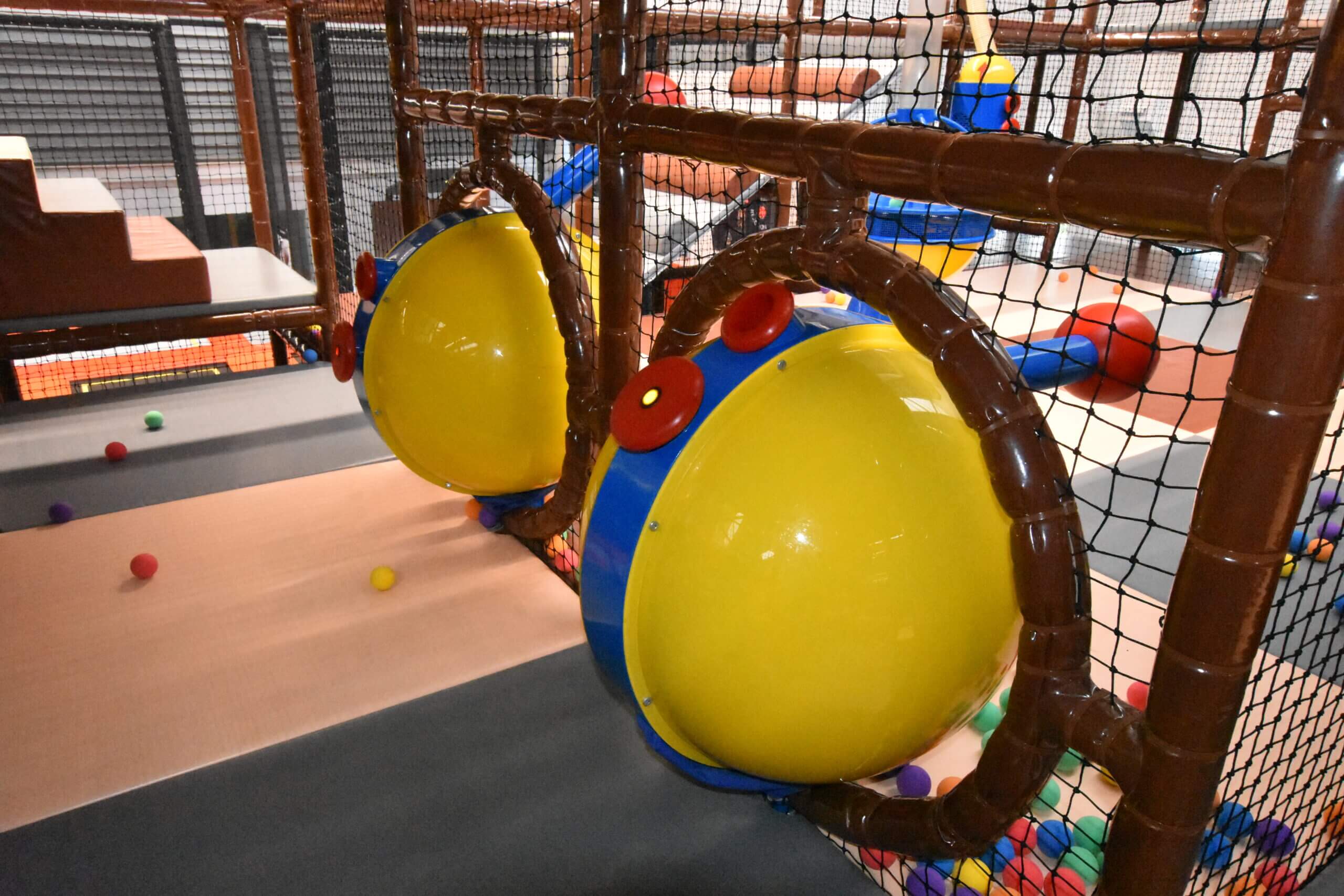 Deux canons à balles interactifs jaunes et bleus intégrés et sécurisés dans une structure de jeux tubulaire, une attraction incontournable pour parc de loisirs indoor.