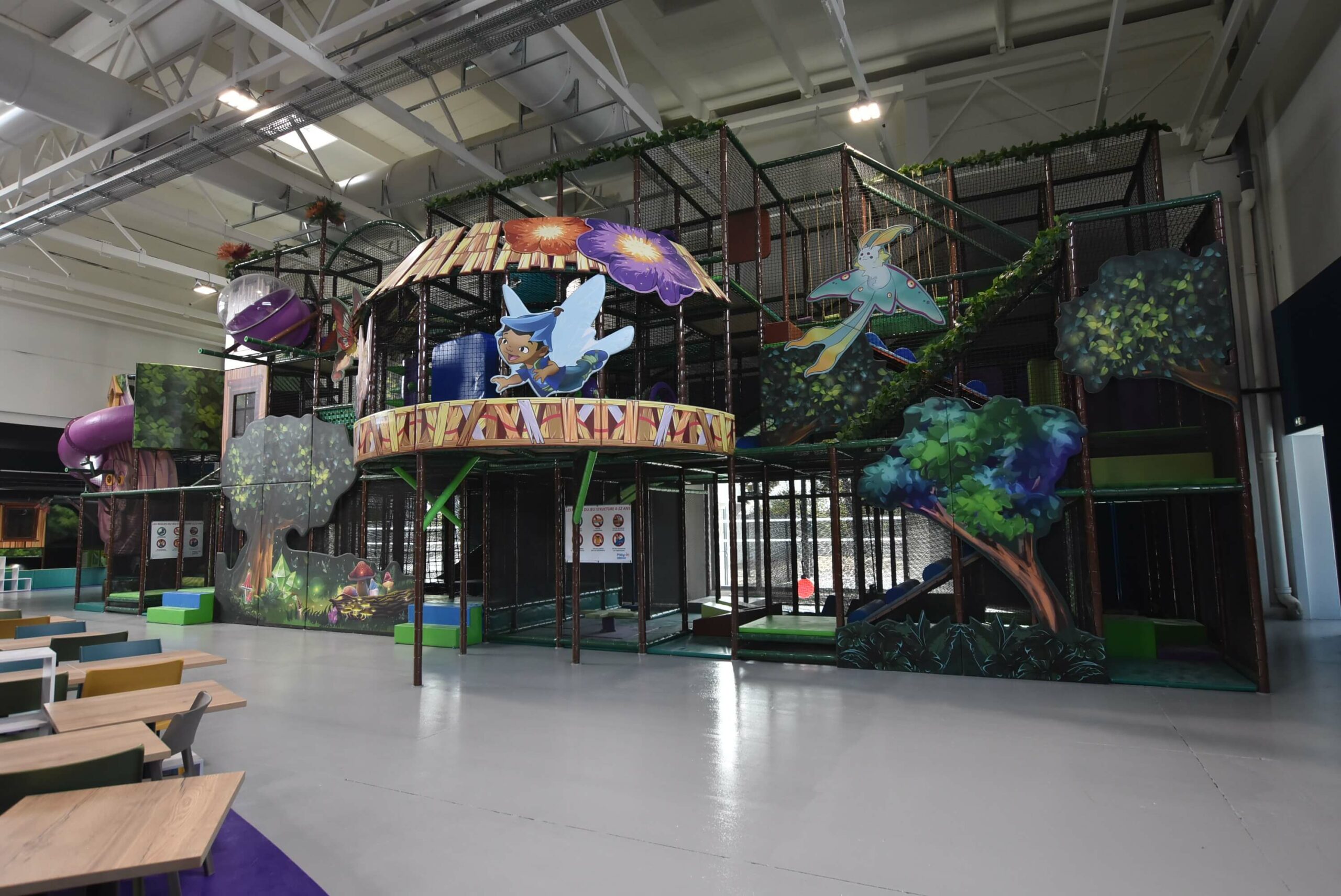 Vue de face de la structure de jeux tubulaire "L'Arbre Magique" sur le thème de la forêt chez Cap2fun à Sélestat. Aménagement Play In Business comprenant des décors d'arbres géants, des ponts en filet et un grand toboggan rouge.