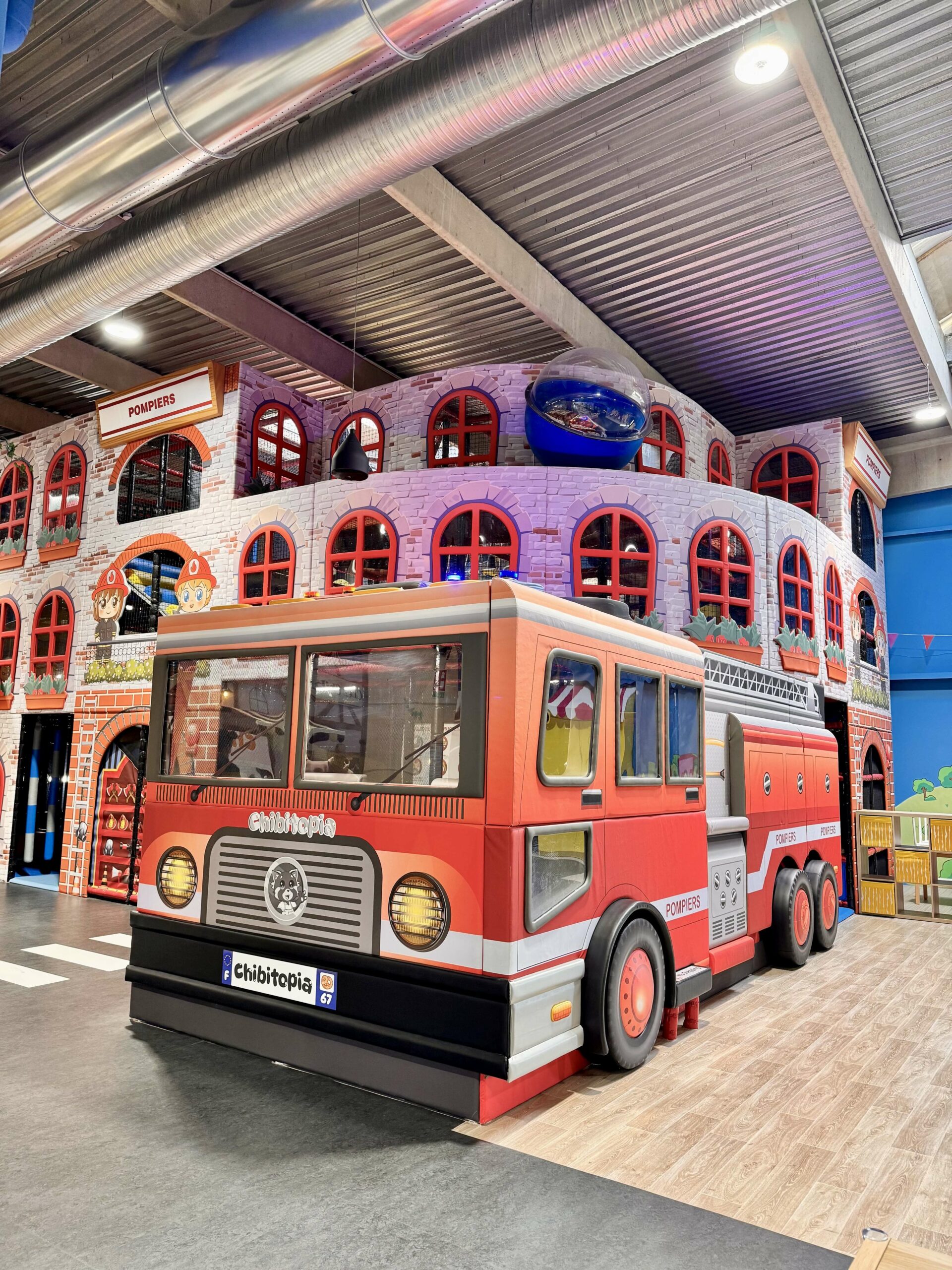 Détail de l'espace de motricité souple Chibitopia conçu par Play In Business : on y voit une piscine de cubes de mousse multicolores, des marches rembourrées jaunes et bleues, des tunnels en filet, et un petit camion jouet rouge en mousse posé près des blocs.