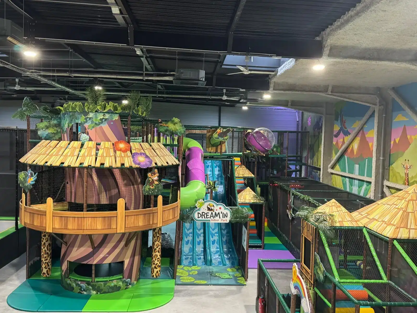 Plaine de jeux indoor géante sur le thème de la jungle avec cabanes perchées et toboggans, conçue et installée sur mesure par Play In Business pour le Dream'In Indoor Park.