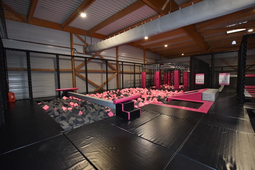 Zone de Trampoline Park au design noir et rose avec grand bac à mousse, poutre de combat (battle beam) et parcours Ninja, aménagée par Play In Business pour le complexe Fun Space à Sens.