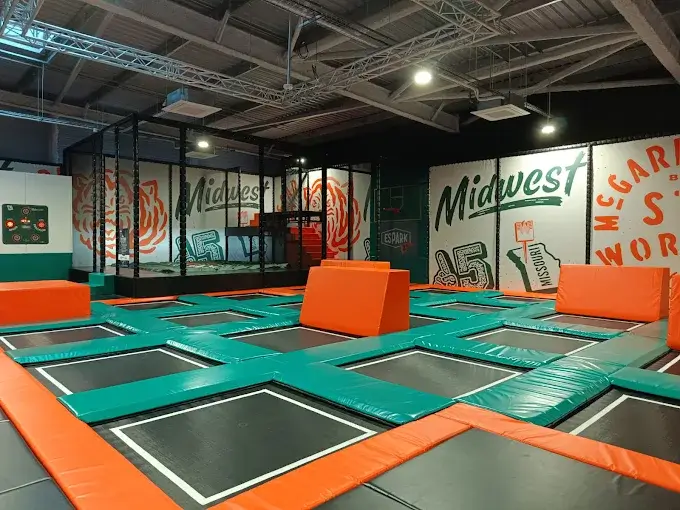 Zone de Trampoline Park sur-mesure avec toiles de saut interconnectées, blocs de franchissement en mousse et décoration thématique sportive, réalisée par Play In Business chez Espark 23.