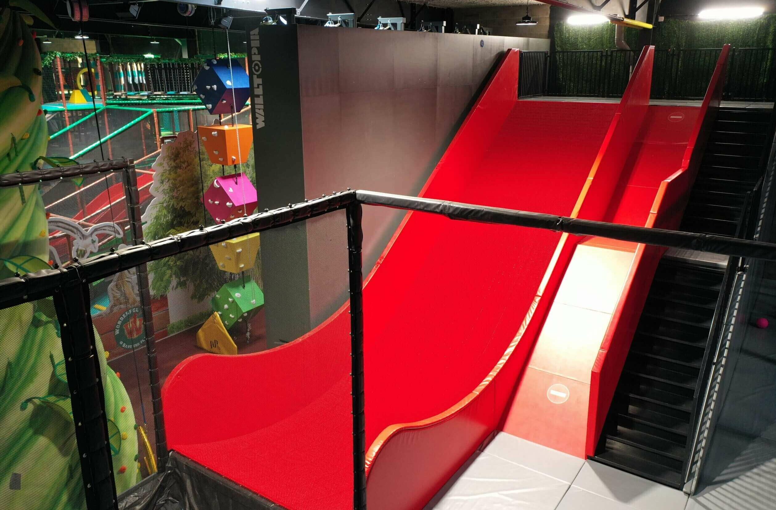 Grand toboggan rouge et modules d'escalade parfaitement intégrés dans un espace atypique, prouvant la capacité de Play In Business à s'adapter aux contraintes de votre bâtiment.