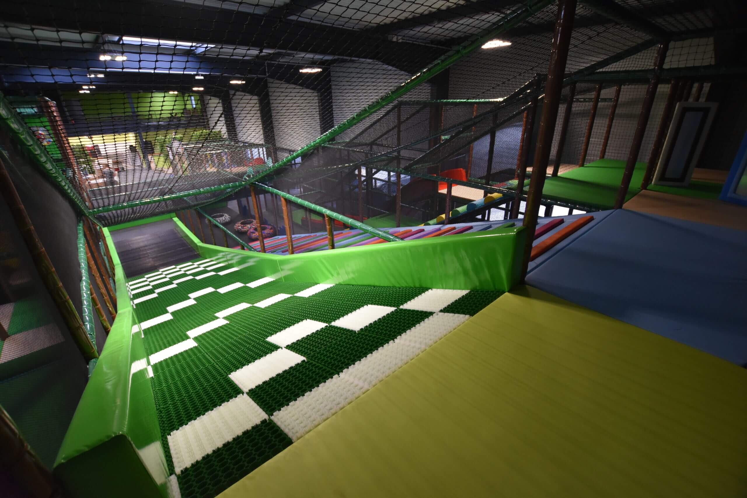 Vue plongeante depuis le sommet du Donuts Slide, une piste de luge indoor avec un revêtement synthétique vert et blanc, sécurisée par des mousses et des filets dans un parc de loisirs couvert.