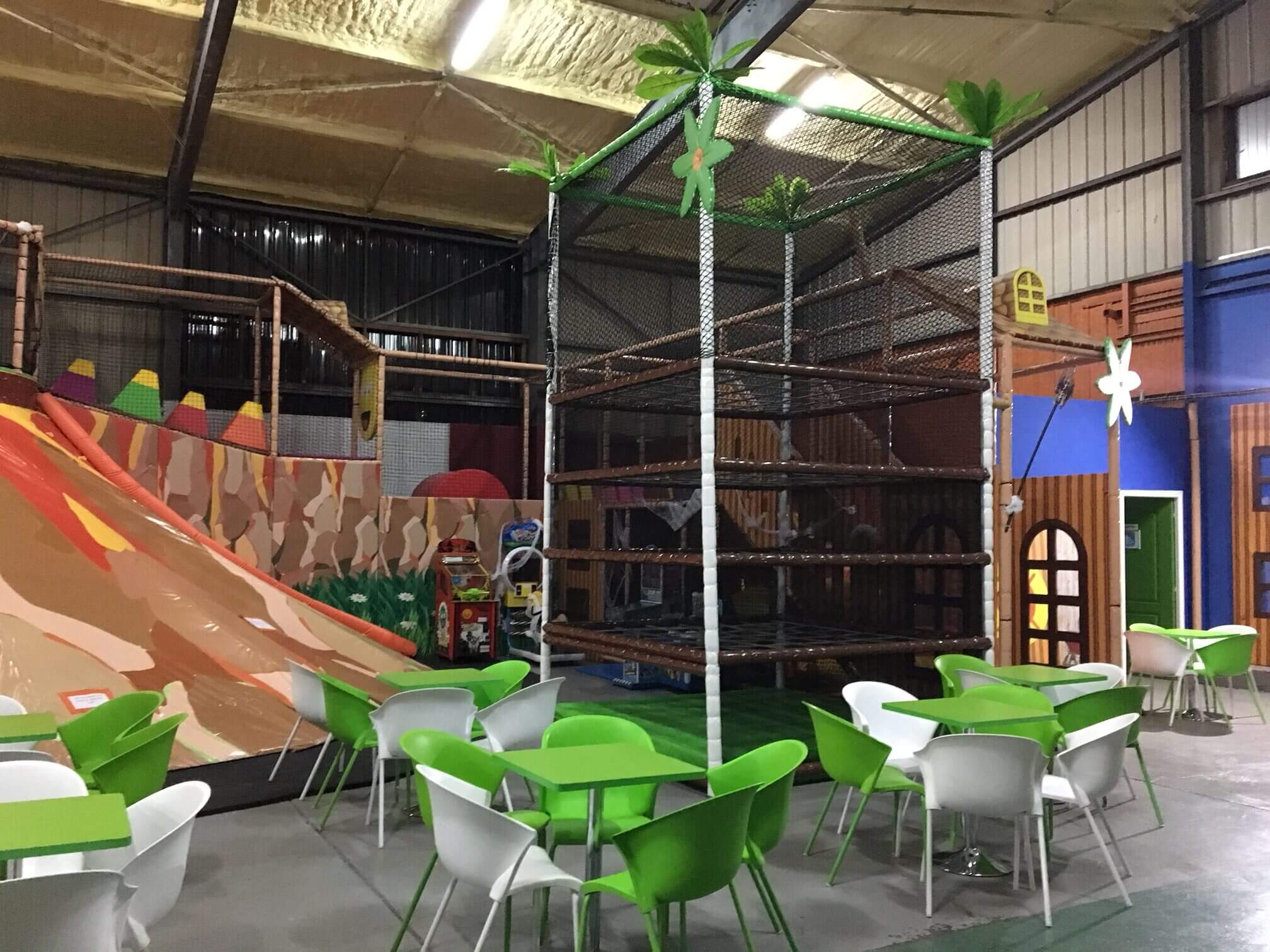 Vue depuis l'espace cafétéria du parc Happy Kids à Saint-Pierre, montrant une tour de grimpe en filets sur-mesure et un décor de volcan, aménagés par Play In Business.