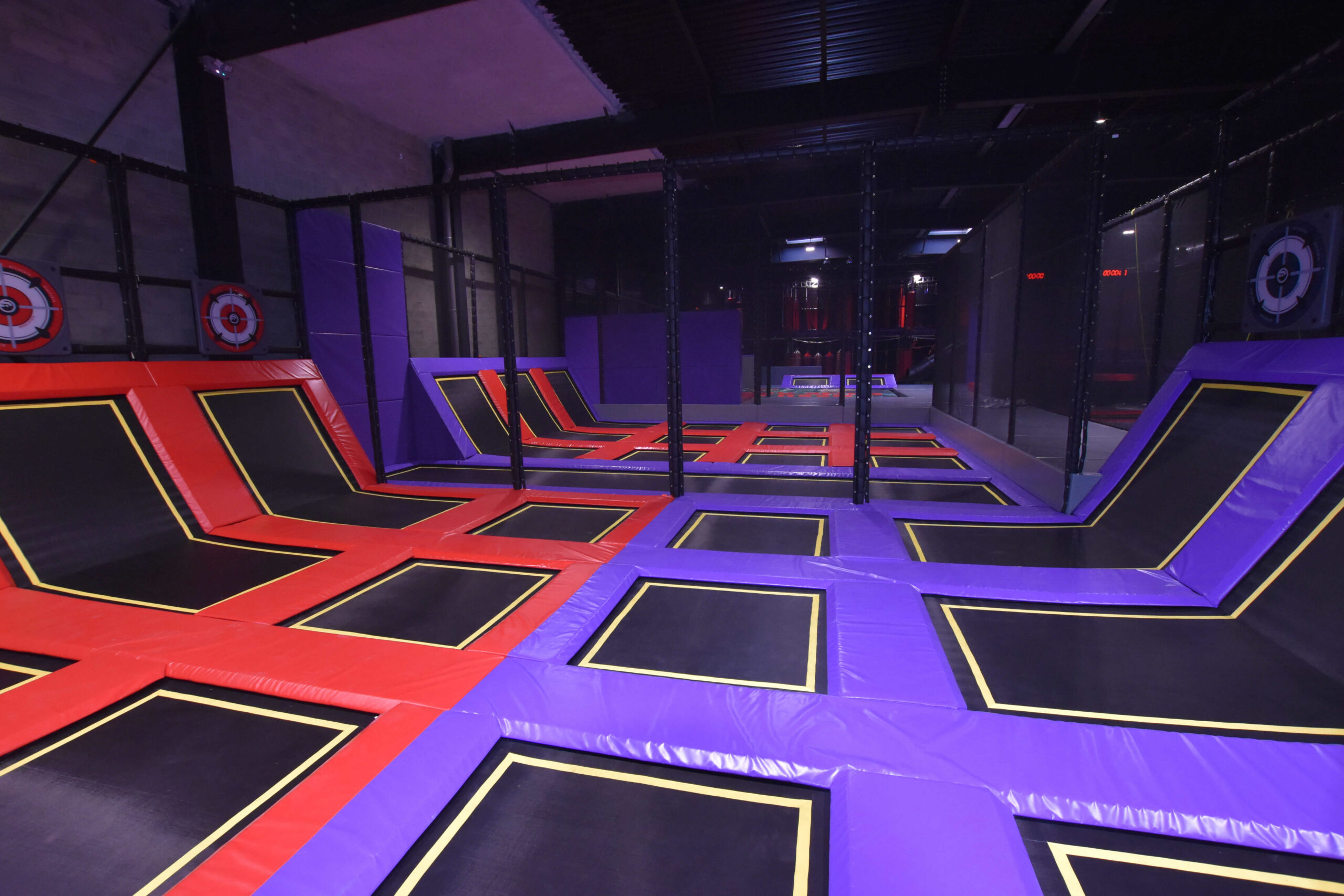 Vaste zone de saut d'un trampoline park indoor avec des toiles violettes et rouges, conçu et installé sur-mesure par Play In Business.