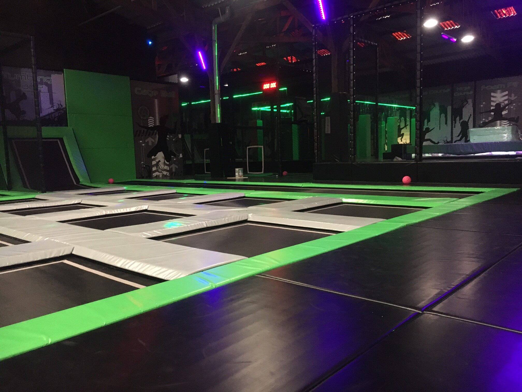 Zone de saut principale du Trampoline Park Jump Park 276 au Thuit-de-l'Oison, avec un design immersif noir et vert fluo, aménagée sur-mesure par Play In Business.