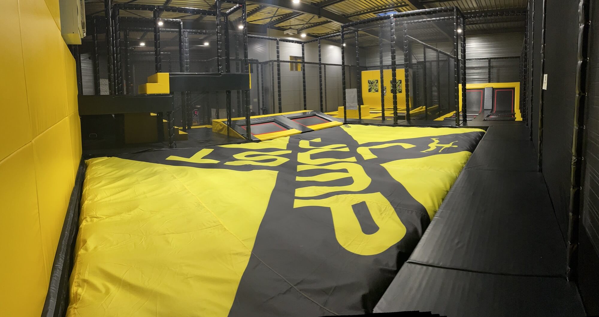 Vue panoramique du Trampoline Park Just Jump à Marnaz avec airbag de réception géant jaune et noir et structure Ninja, conçu et installé par Play In Business.
