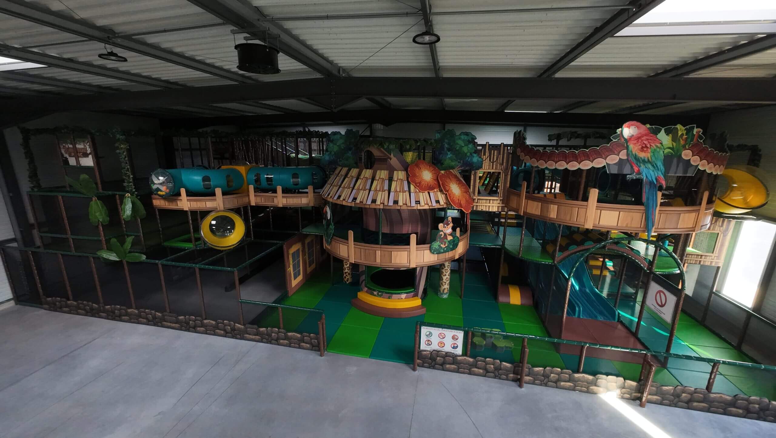 Vue aérienne panoramique d'un grand parc de loisirs indoor multi-activités réalisé par Play In Business. La structure comprend plusieurs niveaux, toboggans géants, filets et zones de jeux colorées.