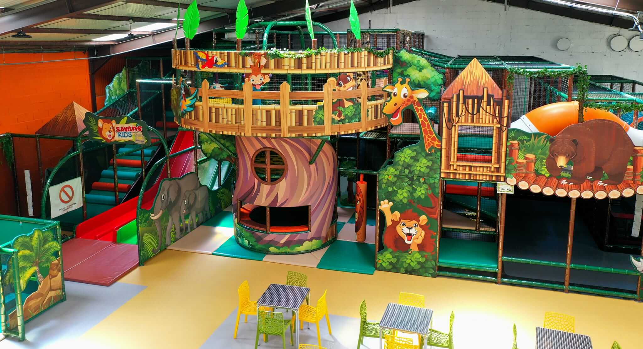 Vue d'ensemble de la plaine de jeux sur le thème de la savane chez Savane Kids à Poilly-lez-Gien. Aménagement Play In Business montrant une structure tubulaire avec une cabane perchée, des décors d'animaux sauvages et un espace détente au premier plan.
