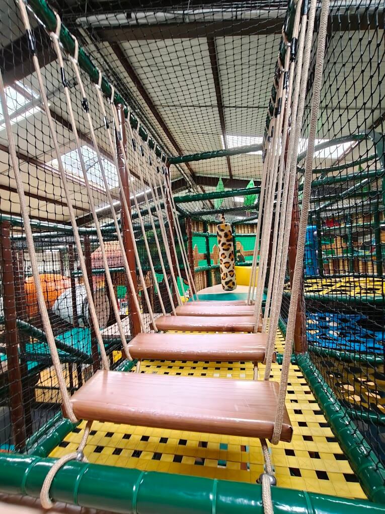Vue intérieure d'un pont de singe suspendu en bois dans la structure de jeux de Savane Kids à Poilly-lez-Gien. Réalisation Play In Business parfaitement sécurisée avec des filets de protection de chaque côté.