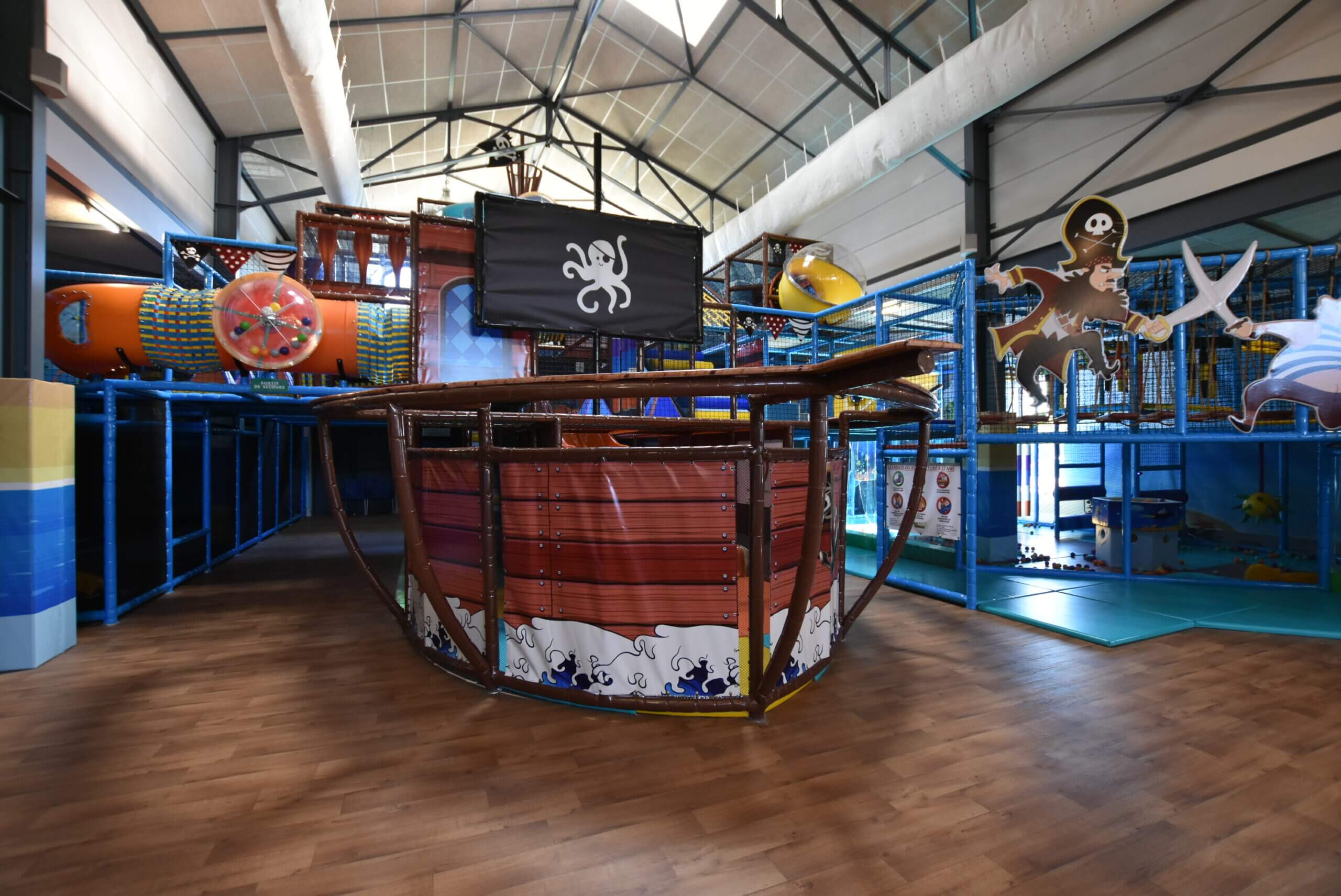 Grande plaine de jeux indoor tubulaire sur le thème des pirates avec décor de navire sur-mesure et toboggan, conçue et installée par Play In Business pour le complexe Hissého à Saint-Mitre-les-Remparts.