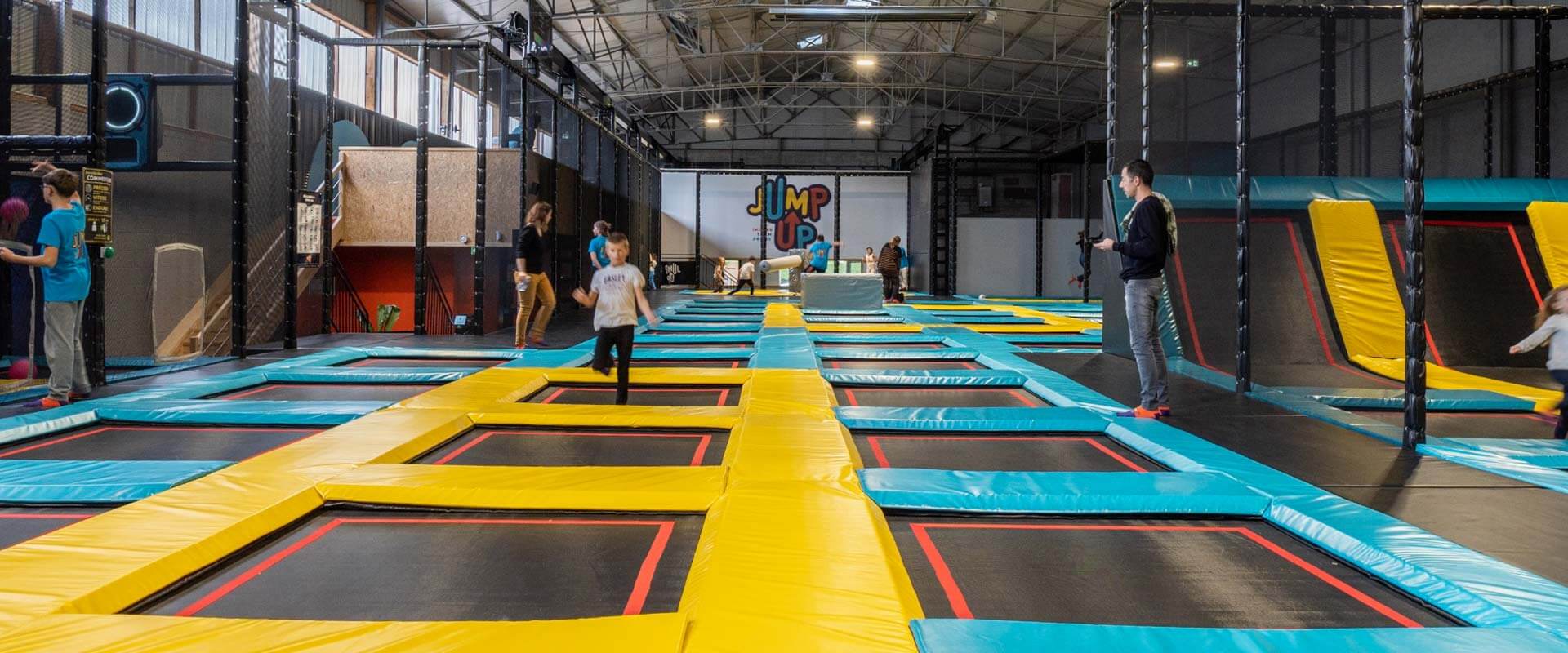 Détail des attractions du parc Jump Up Cherbourg installées par Play In Business : plateforme de saut avec Airbag de réception, trampoline haute performance Wall Rider et zone de Basketball, thématique orange et bleu.