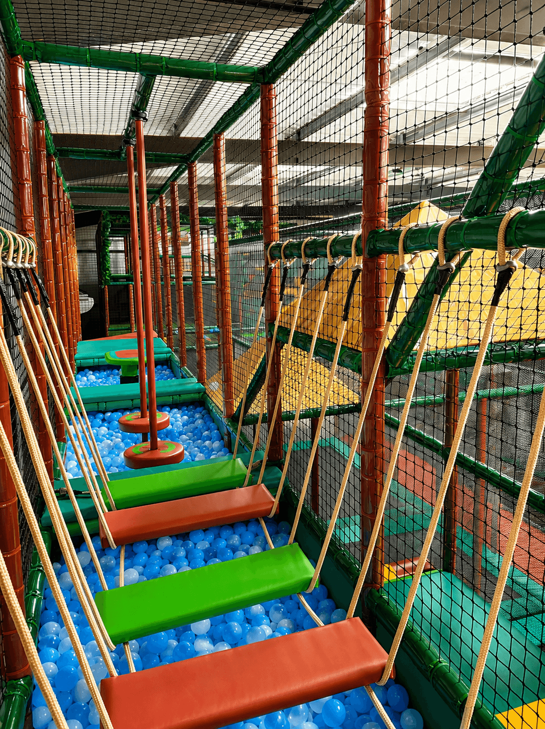 Intérieur de la structure de jeux Wistitiparc à Saint-Pierre-lès-Elbeuf : parcours d'obstacles avec pont de singe suspendu au-dessus d'une piscine à balles bleues et blanches, aménagement Play In Business.