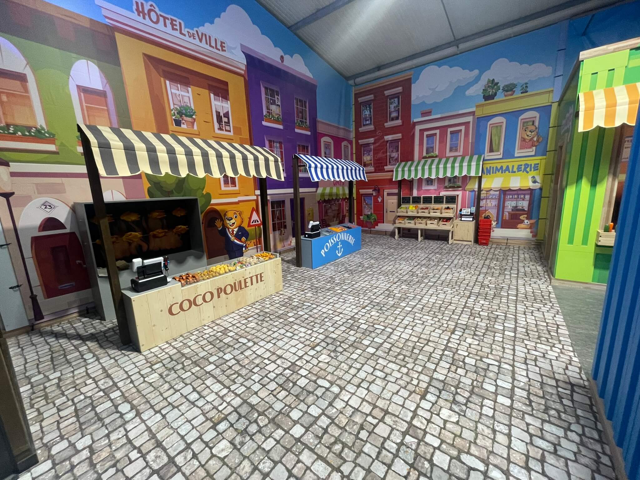 Village de jeux d'imitation avec marché et décors urbains pour parc de loisirs indoor.