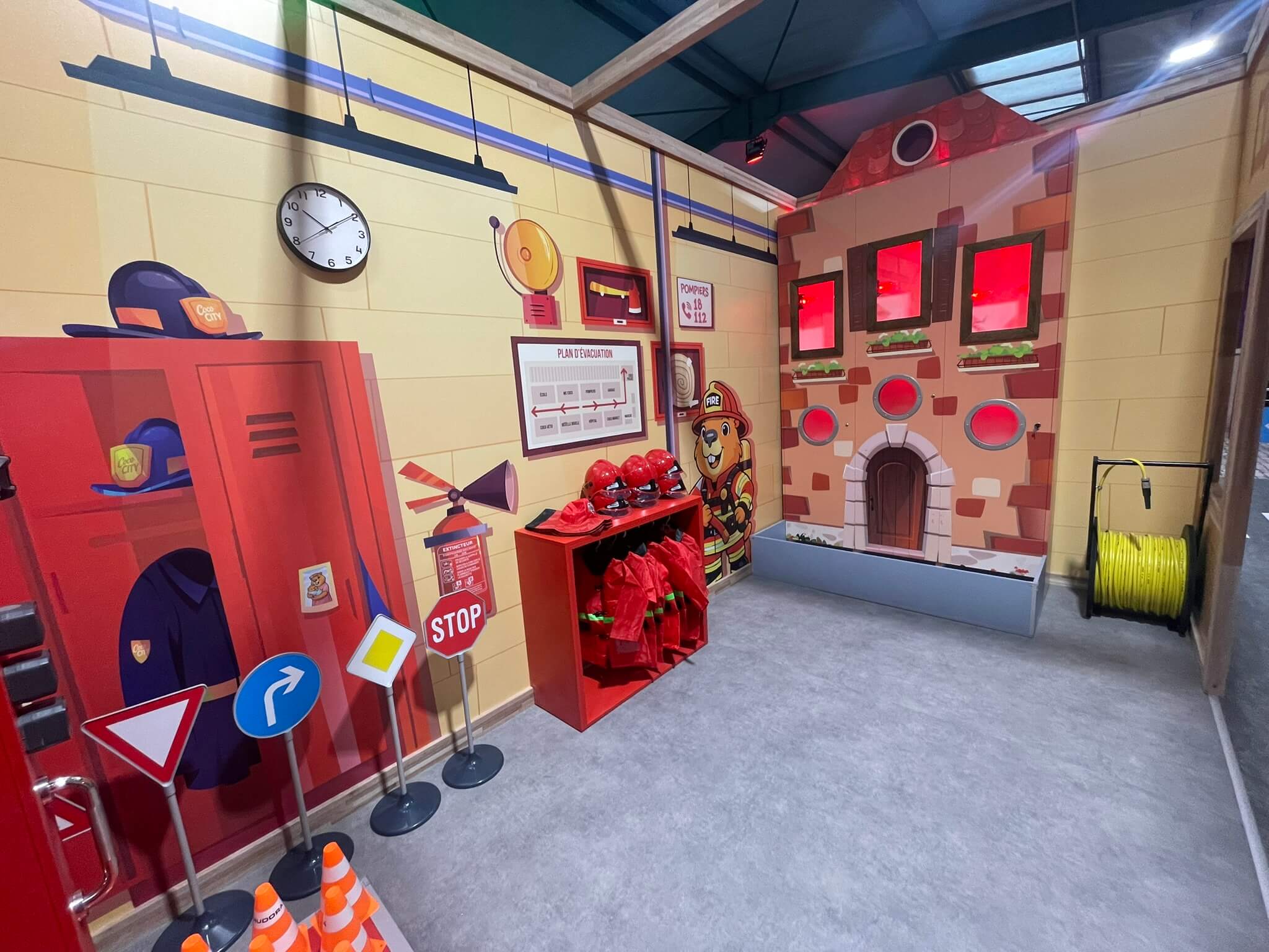 Intérieur du jeu d'imitation caserne de pompiers avec casques, vestes et maison en feu pour parc indoor.