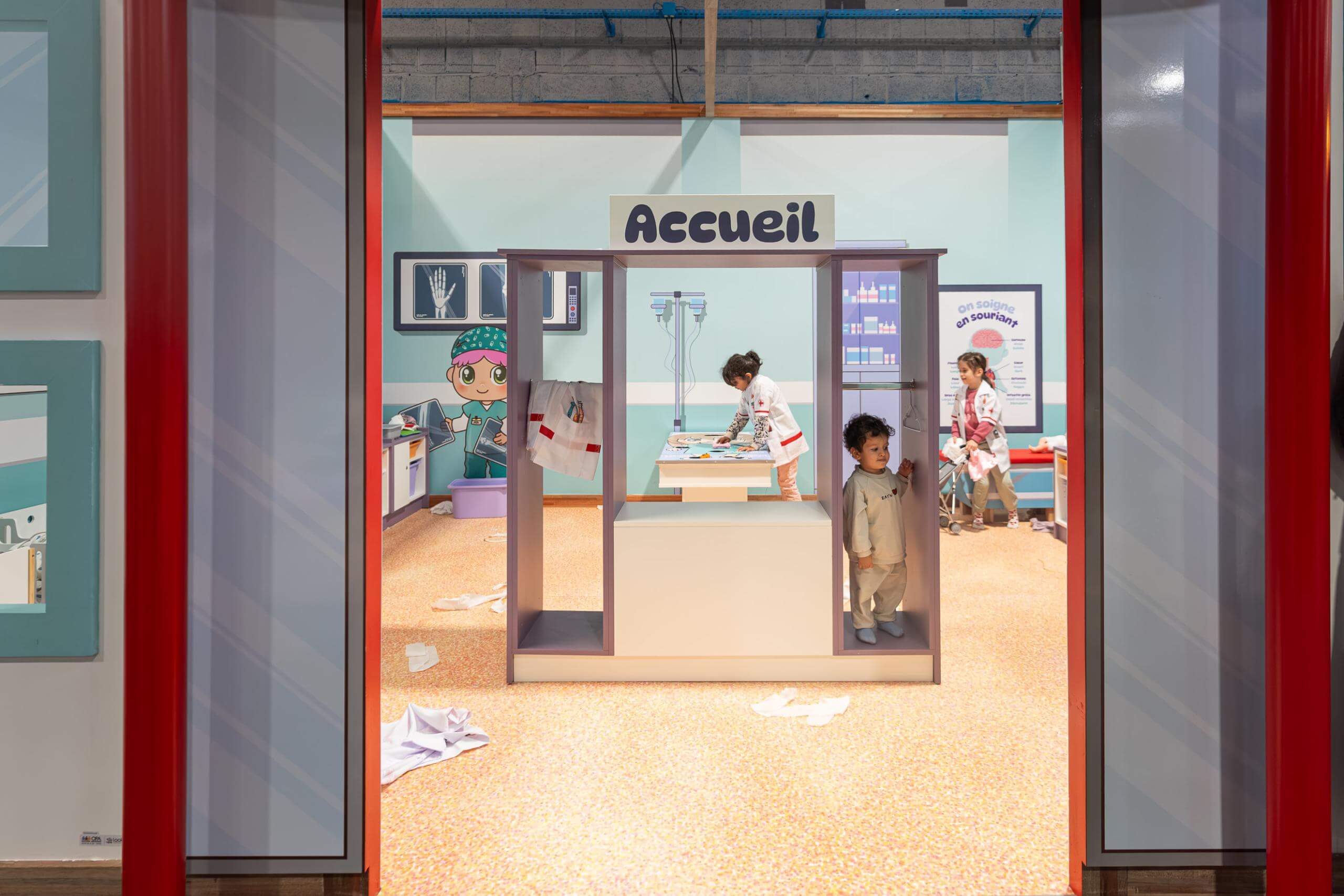 Jeu d'imitation hôpital avec meuble d'accueil, décors médicaux et enfants en blouse pour parc de loisirs indoor.